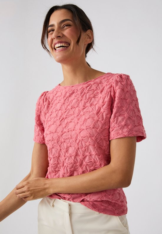 Mannequin souriant portant un t-shirt rose à manches courtes bouffantes et motif gaufré.