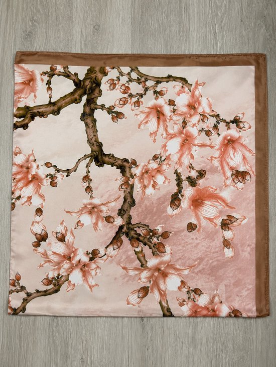 Vierkante zijden sjaal met bruine rand en roze magnoliabloesems op een houten ondergrond.