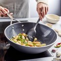 Zwarte wokpan waarin groenten en vlees worden gebakken.