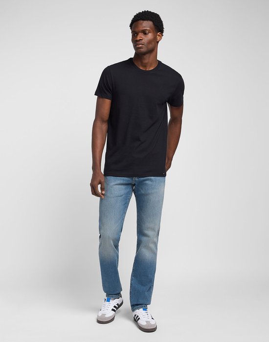 Man met een zwarte T-shirt en lichtblauwe spijkerbroek, met witte sneakers met blauwe en grijze details.
