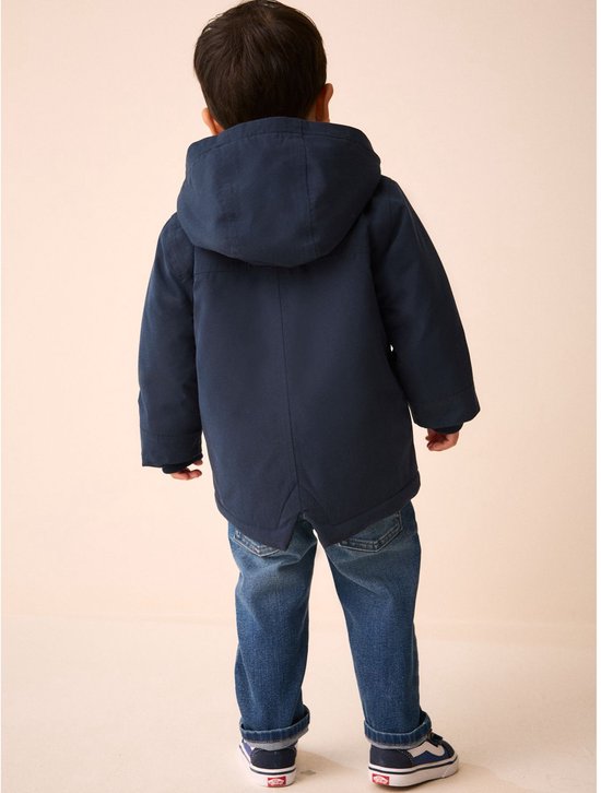 Jongetje in donkerblauwe parka en spijkerbroek, van achteren gezien.