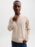Man, lichtbeige gebreid poloshirt met lange mouwen, twee zwarte knoopjes en donkerblauwe jeans.