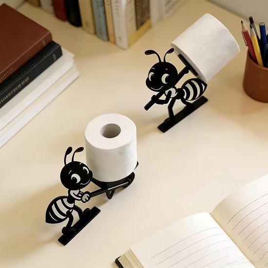 Zwarte ant-vormige toiletrolhouders met rollen op een bureau met boeken en een notitieboek.