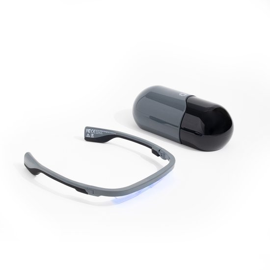 Een AYO-lichttherapiebril en de bijbehorende capsulevormige oplader liggen op een witte achtergrond.