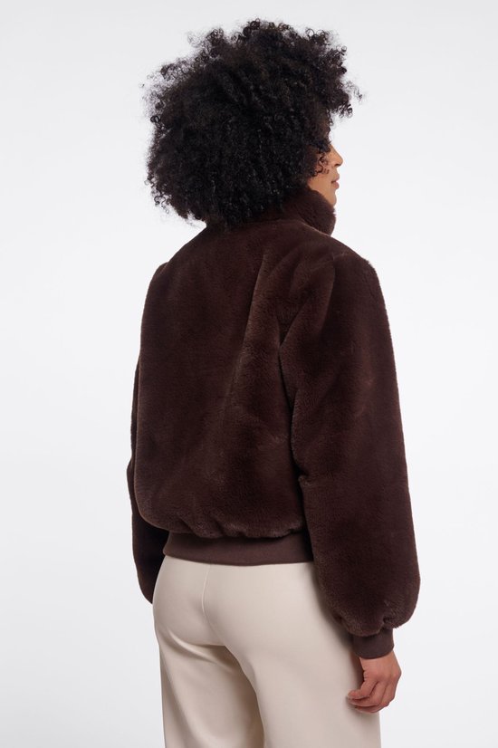 Achterkant van een model met een bruine Faux Fur bomberjack met hoge kraag en leren sluitingen. Ze draagt een lichte broek.