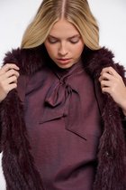Model in donkerrode bont bodywarmer met strikblouse, kijkend naar beneden.