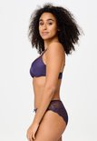 Zijaanzicht van model in een paarse T-shirt bh en slip met kanten zijpanelen.