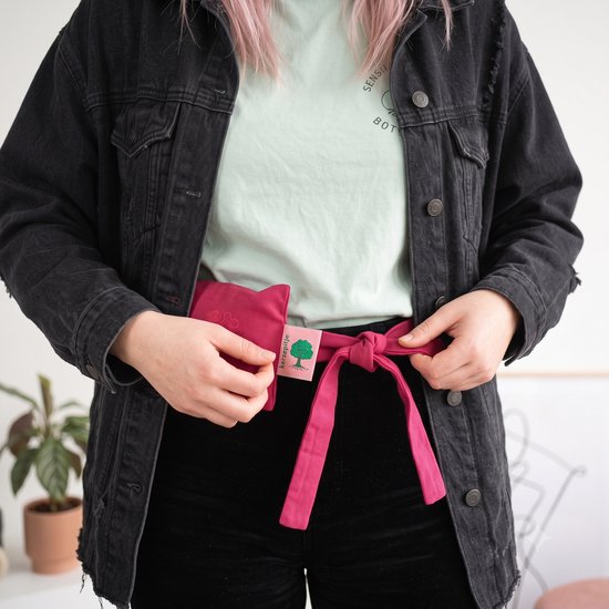 Vrouw met spijkerjasje en lichtgroen T-shirt knoopt een rood warmtekussen om haar middel.