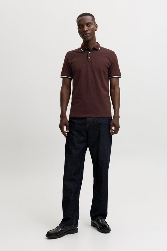 Man draagt bordeauxrode polo met witte en marineblauwe streepdetails, met donkere jeans.