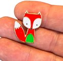 Emaille pin van een vosje met rode vacht, witte snuit en staartpunt, en groene buik, vastgehouden in een hand.