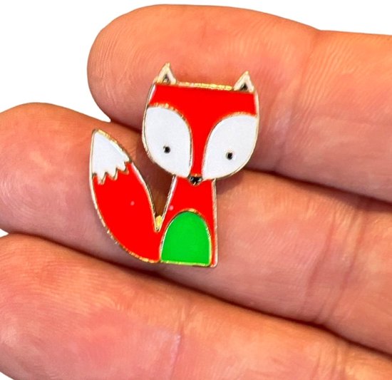 Emaille pin van een vosje met rode vacht, witte snuit en staartpunt, en groene buik, vastgehouden in een hand.