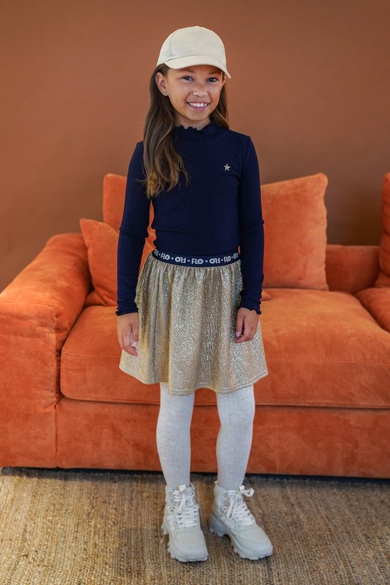 Meisje in donkerblauw ribbel T-shirt met opgestikte roze ster, gouden glitter rok, witte legging en pet.