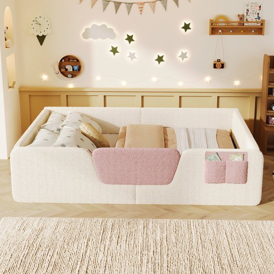 Laag kinderbed van lichtbeige teddy stof met roze accenten, opgemaakt met beddengoed.
