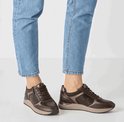 Damesbenen in spijkerbroek met bruine Tamaris sneakers met bronzen accenten.