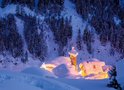 Een besneeuwd bos met verlichte huizen in de schemering.
