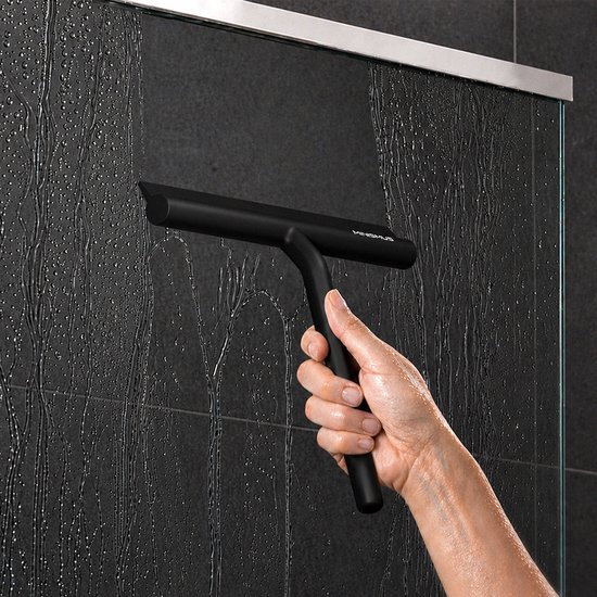 Raclette de douche noire à manche ergonomique, utilisée sur un mur de carrelage noir humide.
