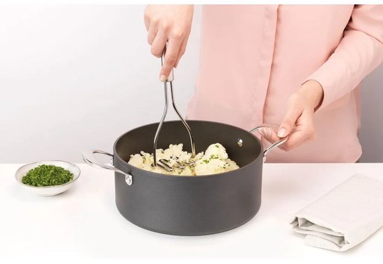 Een persoon stampt aardappelen in een grijze pan met een aardappelstamper van RVS.