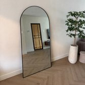 Zwarte, grote boogspiegel staand tegen een muur met een houten vloer.