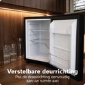 Open lege zwarte BREND koelkast met verstelbare deurrichting, in een keukenomgeving met glazen.