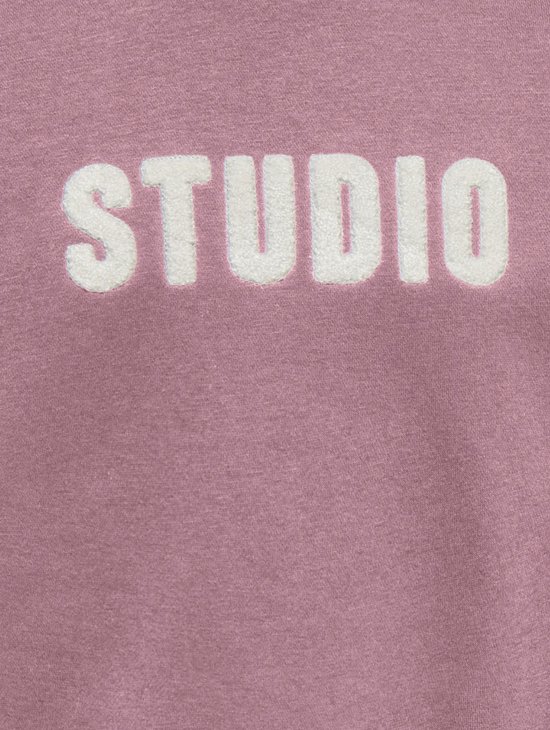 Roze sweater met witte 'STUDIO' tekst op de borst.