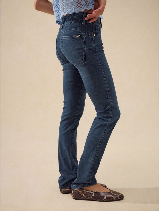 Model in een lichtblauwe kanten top en donkerblauwe slim jeans met rechte pijpen.