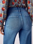 Achterkant van een model in een blauwe top met appelprint en gele ruit, met een hoge taille en wijde jeans.