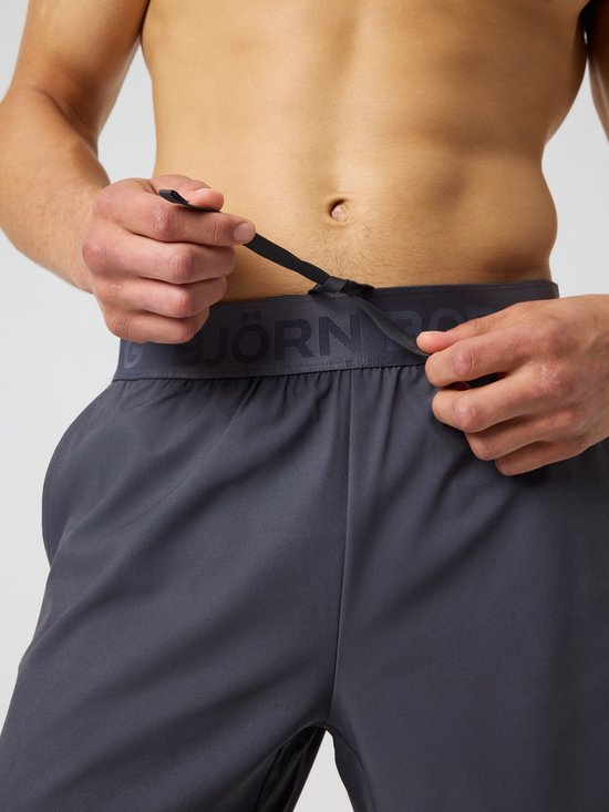 Donkere grijze sportbroek met trekkoord en logo op de tailleband.