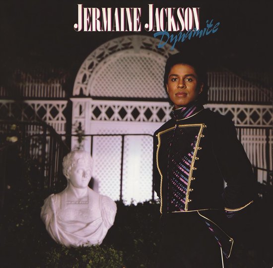Jermaine Jackson in een zwart jasje met gouden versieringen en een paarse en roze band. Naast hem staat een wit bustebeeld.