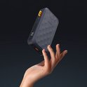 Hand houdt een donkergrijze Xtorm powerbank omhoog. Powerbank heeft honingraatpatroon en digitaal display.