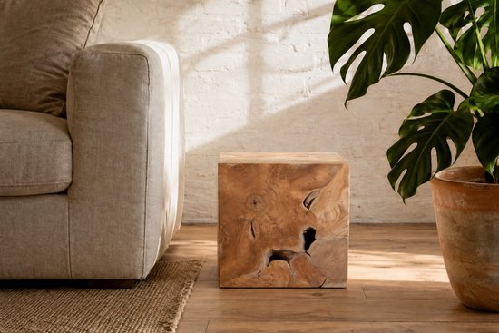Kubus van teakhout met unieke knoesten en houtnerfstructuur, naast een beige bank.