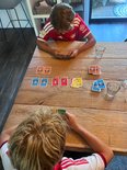 Twee jongens met rode en witte voetbalshirts spelen kaartspel aan een houten tafel. Kaarten met voetballers.