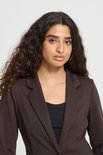Close-up van een vrouw met krullend haar, draagt een bruine blazer over een zwarte top.