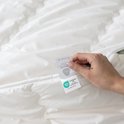 Hand houdt Oeko-Tex label vast op een wit, gewatteerd wollen dekbed.