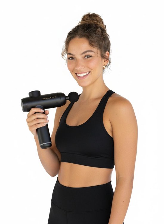 Glimlachende vrouw met spierballen, houdt zwarte MusclePro massage gun in haar rechterhand. Ze draagt zwarte sportkleding.