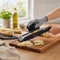 Hand snijdt pastinaak met zwarte mandoline snijder. Fijngesneden pastinaak, plakjes en staafjes. Olijfolie, kruidenplantje.
