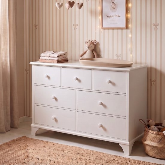 Witte commode met zeven laden, in een kinderkamer met gestreepte behang.