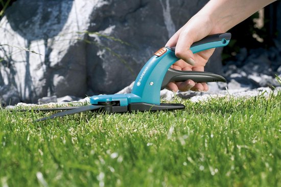 Blauwe Gardena graschaar met oranje knop, gebruikt in gras.