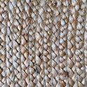 Close-up van de vlechtstructuur van een rond jute vloerkleed in natuurlijke tinten.
