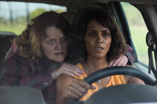 Halle Berry kijkt angstig achter het stuur, terwijl een vrouw haar hand op haar schouder legt.