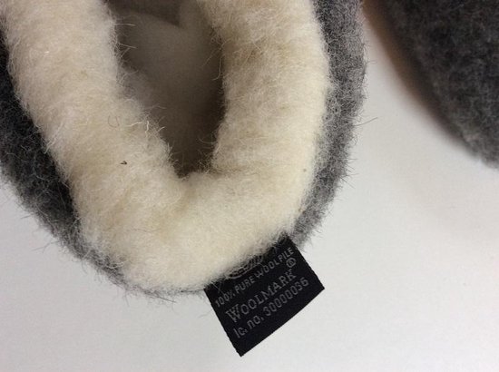 Detail van de binnenkant van grijze wollen sloffen met witte vacht en Woolmark label.