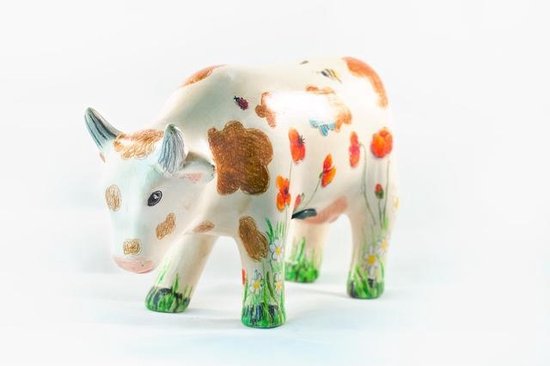 Keramische koe versierd met bloemen, vlinders en bruine vlekken.
