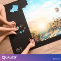 Kinderhanden die puzzelstukjes aanleggen op een zwarte puzzelmat met een landschap met luchtballonnen.