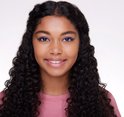 Jong meisje met krullend haar, draagt een roze shirt. Blauwe eyeliner op haar oogleden.