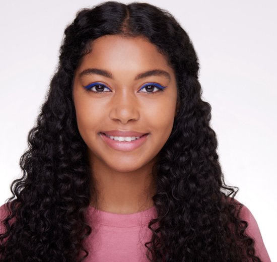 Jong meisje met krullend haar, draagt een roze shirt. Blauwe eyeliner op haar oogleden.