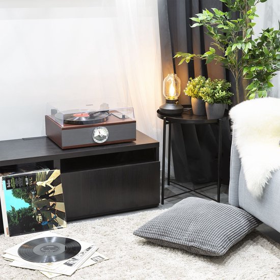Retro platenspeler op een donkere kast in een woonkamer, met vinylplaten op de grond.