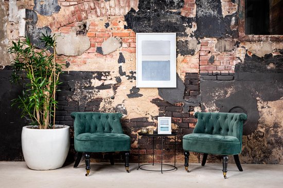 Moderne woonkamer met twee groene fluwelen stoelen en een ingelijste abstracte print aan een bakstenen muur.