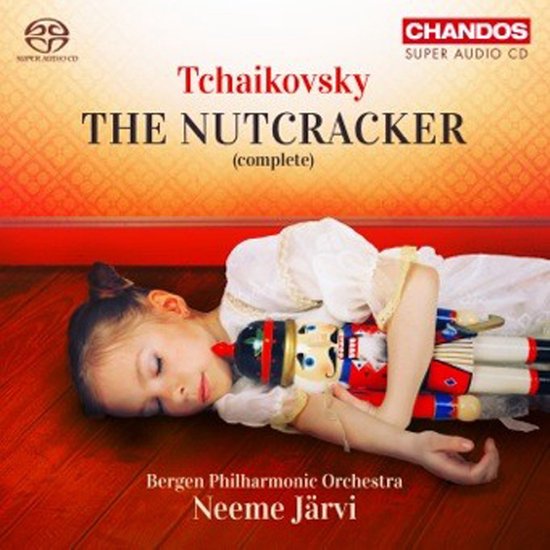Een meisje in een wit balletpakje slaapt op een houten vloer, met een notenkrakerpop in haar armen. Tekst: Tchaikovsky The Nutcracker (complete).