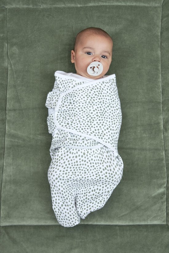 Baby ingebakerd in een doek met groene stipjesprint, liggend op een groen kleed.