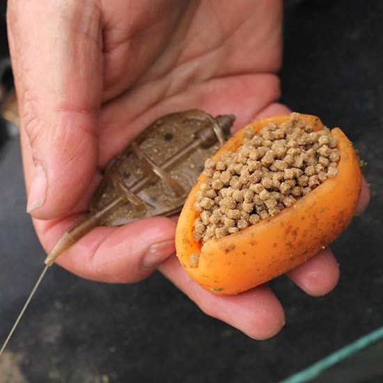 Une main tient un moule de pêche orange rempli de granulés et d'une petite bouillette rouge.