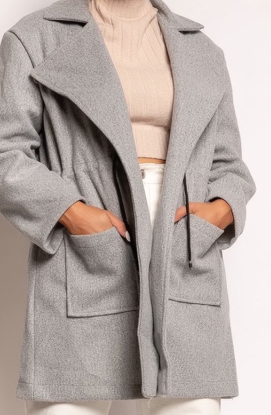 Lichtgrijze jas met opstaande kraag, trekkoord aan de taille, en opgestikte zakken. Model draagt een beige coltrui en witte broek.